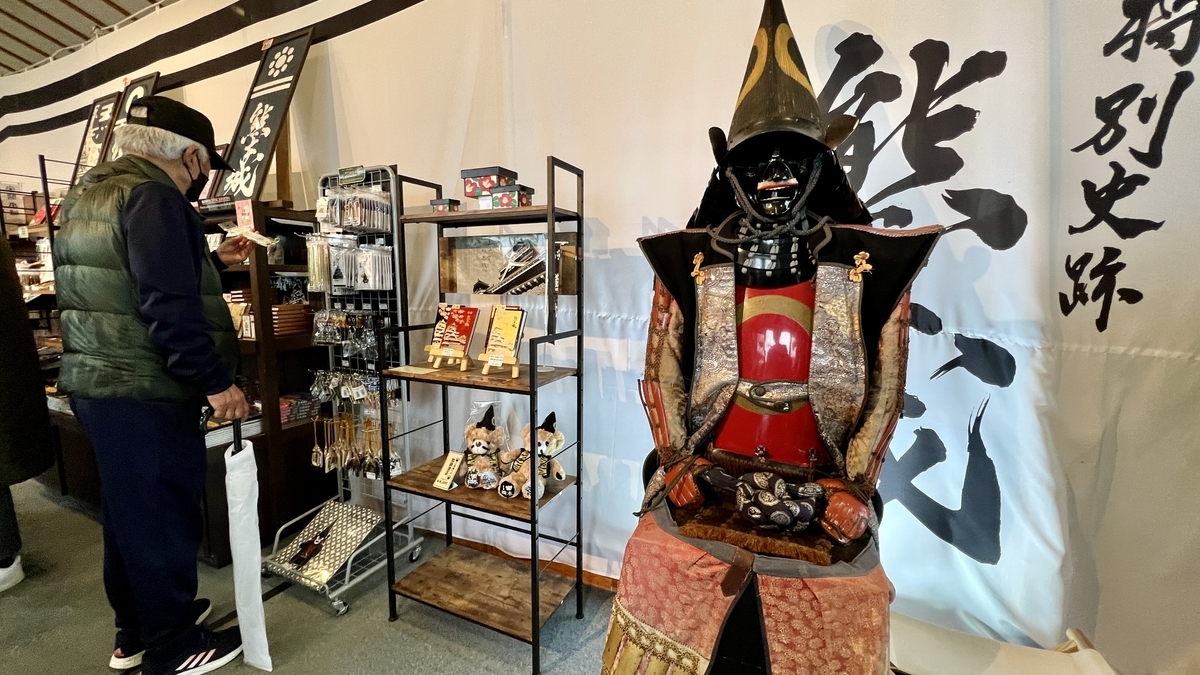 구마모토성 매점 내 무사 갑옷 전시와 기념품 진열대를 보는 방문객