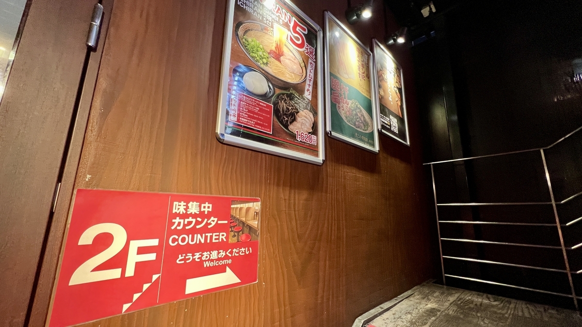 맛 집중 카운터로 안내하는 2층 계단 안내 표시와 벽의 메뉴 사진