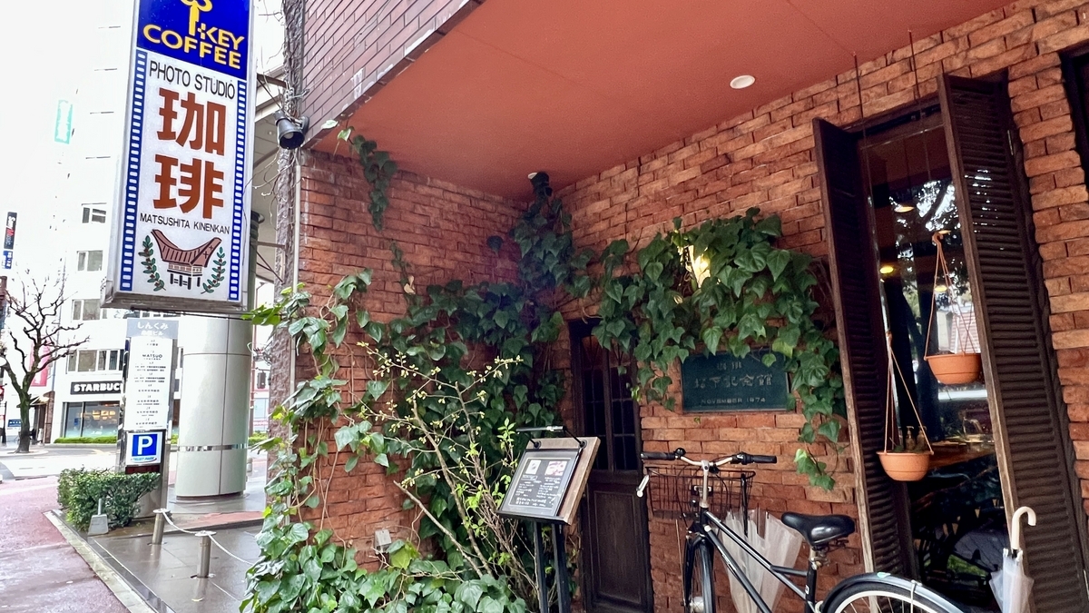 담쟁이덩굴이 감긴 붉은 벽돌 벽과 커피 세로 간판이 표시된 마쓰시타 기념관 입구