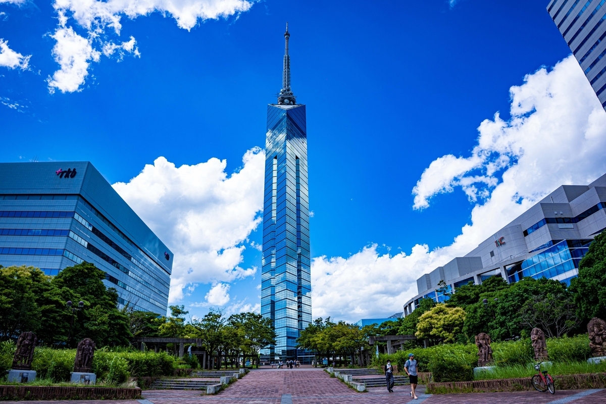 Full view of Fukuoka Tower against blue sky with white clouds and surrounding greenery