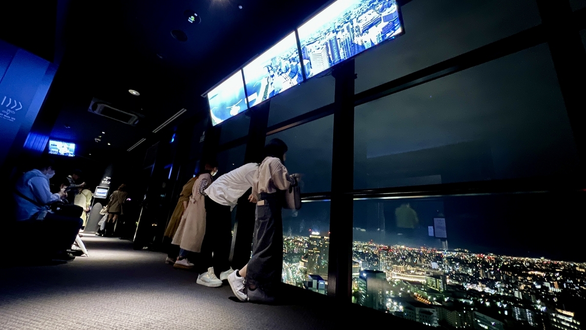 Visitors leaning against the large windows overlooking Fukuoka city night view