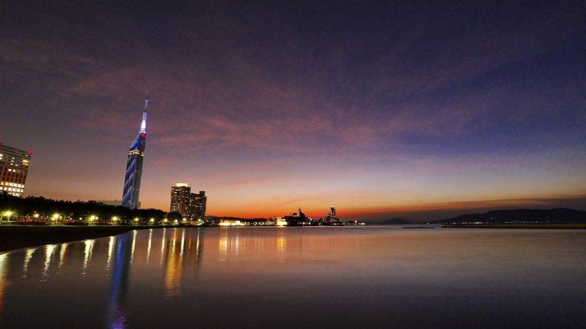Fukuoka Tower blue lights reflected in Hakata Bay at sunset with street lights mirrored on the water