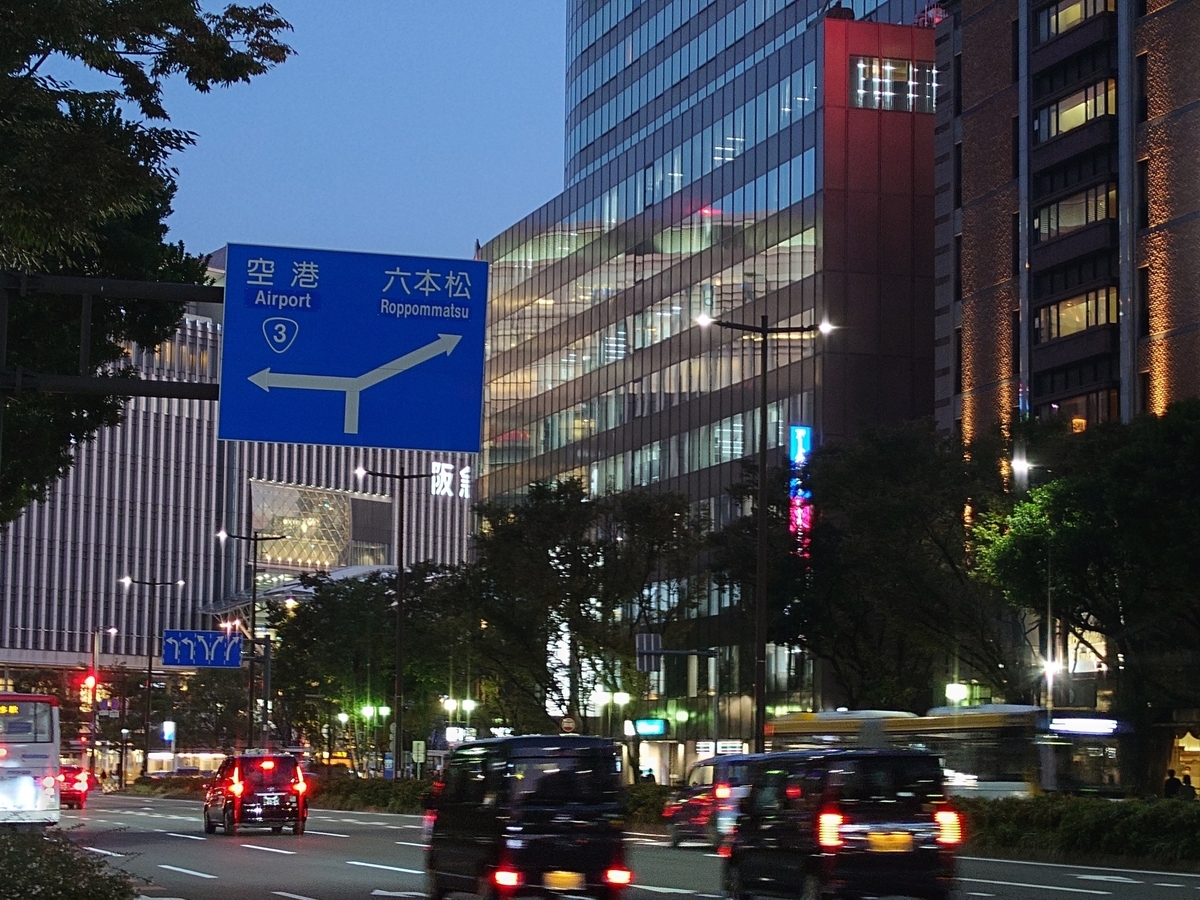 Blue road signs pointing to the airport and Ropponmatsu in the Tenjin area at dusk with traffic