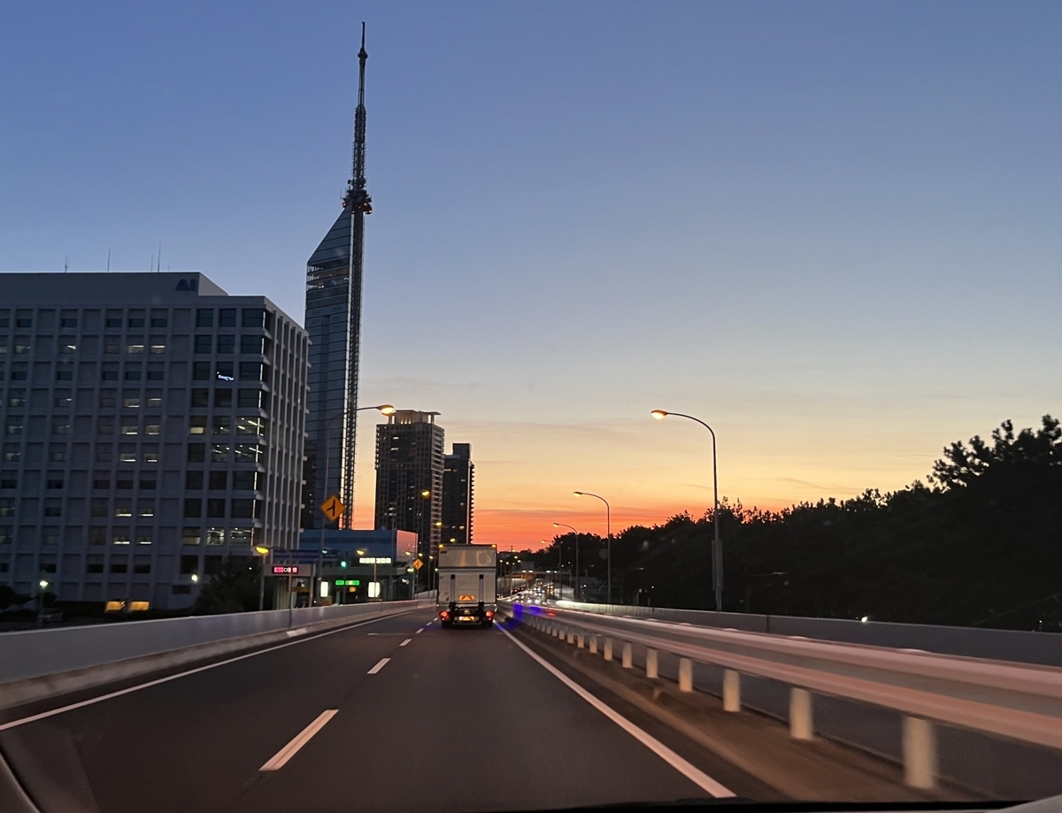 Traffic on the road at dusk with Fukuoka Tower rising ahead