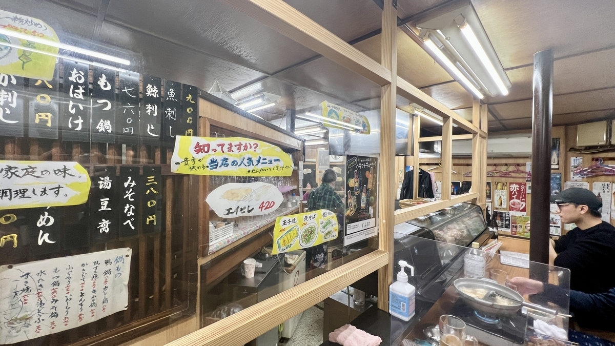 Vista interior mostrando barra con cocina y tiras de menu escritas a mano en division de madera