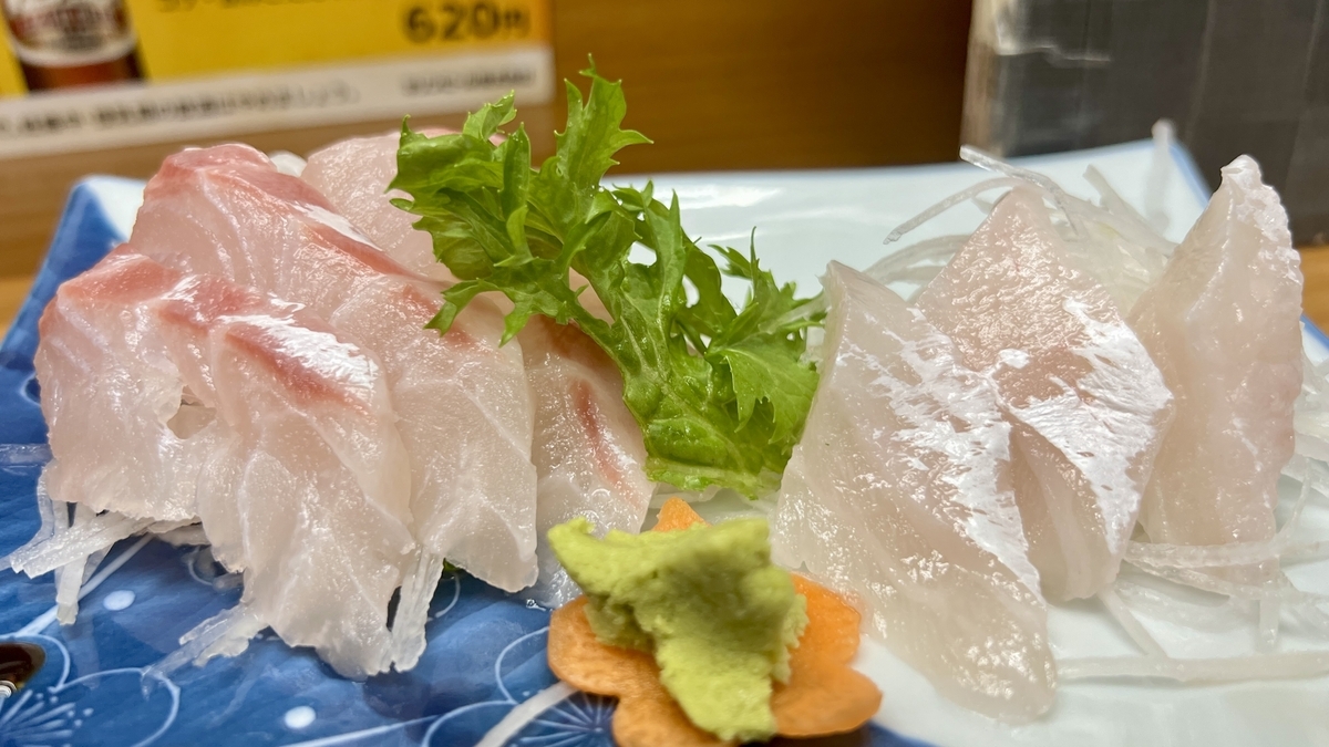 Sashimi de pescado blanco servido en un plato cuadrado azul con wasabi y shiso