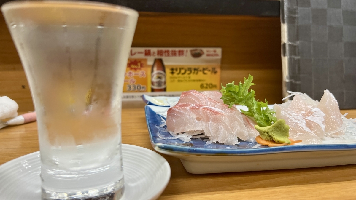 Copa de sake frio y bandeja de sashimi de pescado blanco en la barra