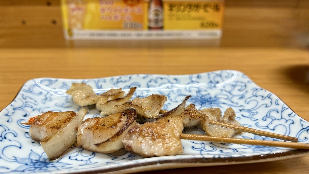 Brochetas de panceta de cerdo y piel de pollo servidas en un plato cuadrado con patron azul