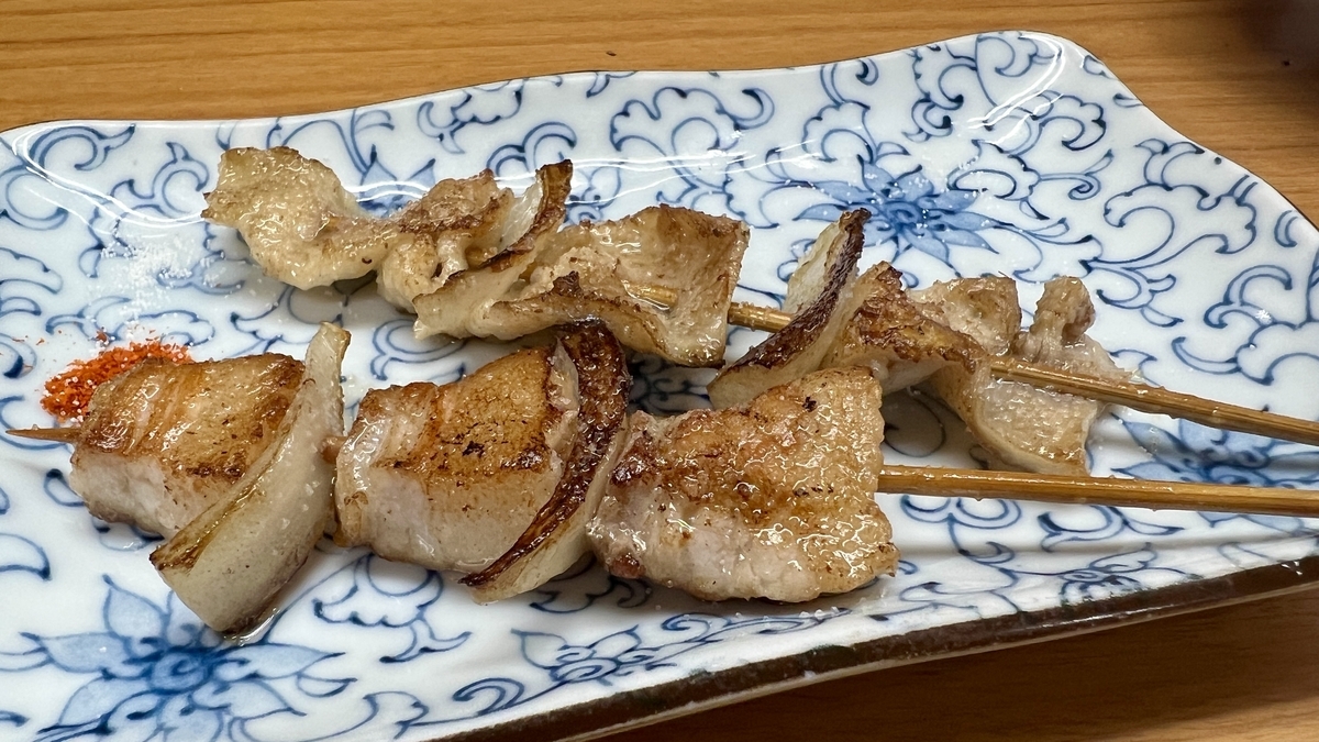 Brochetas de panceta de cerdo y piel de pollo con pimienta shichimi en un plato cuadrado con patron azul