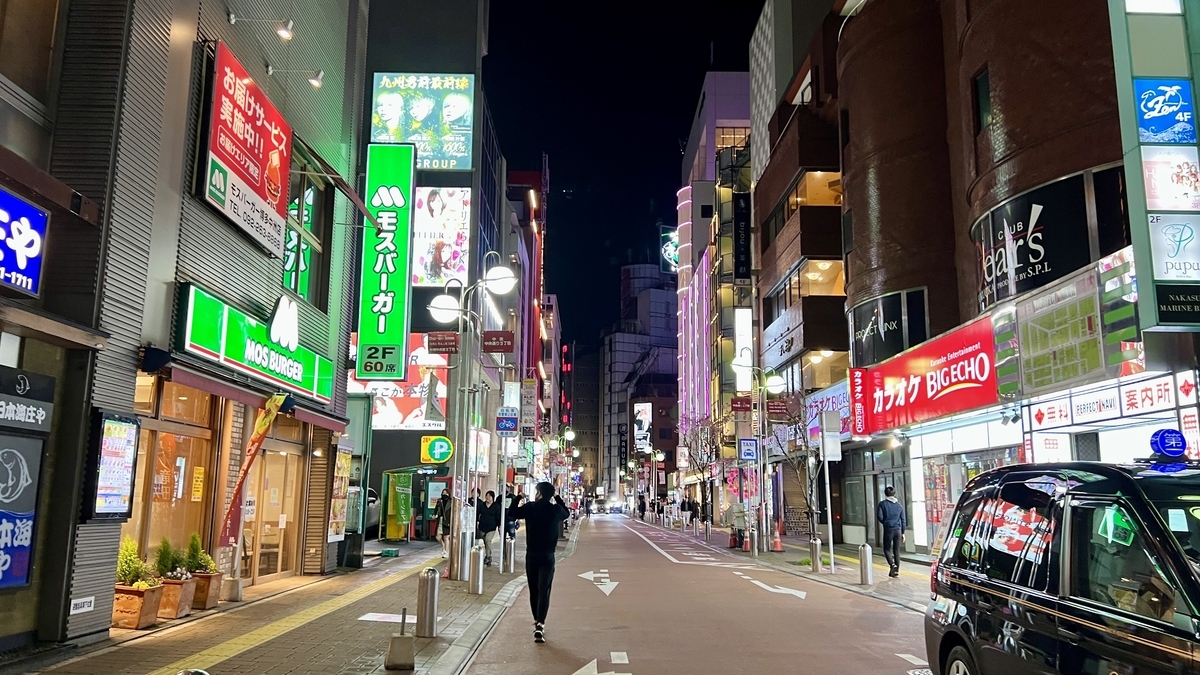 中洲の夜の大通りにモスバーガーやカラオケのネオン看板が並ぶ繁華街の通り