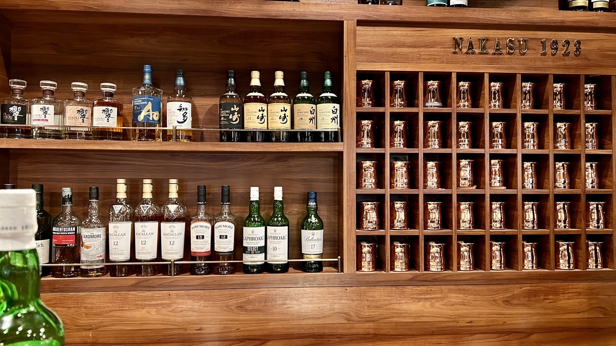 ウイスキーボトルが並ぶ棚と銅製マグが整然と並んだ壁面収納