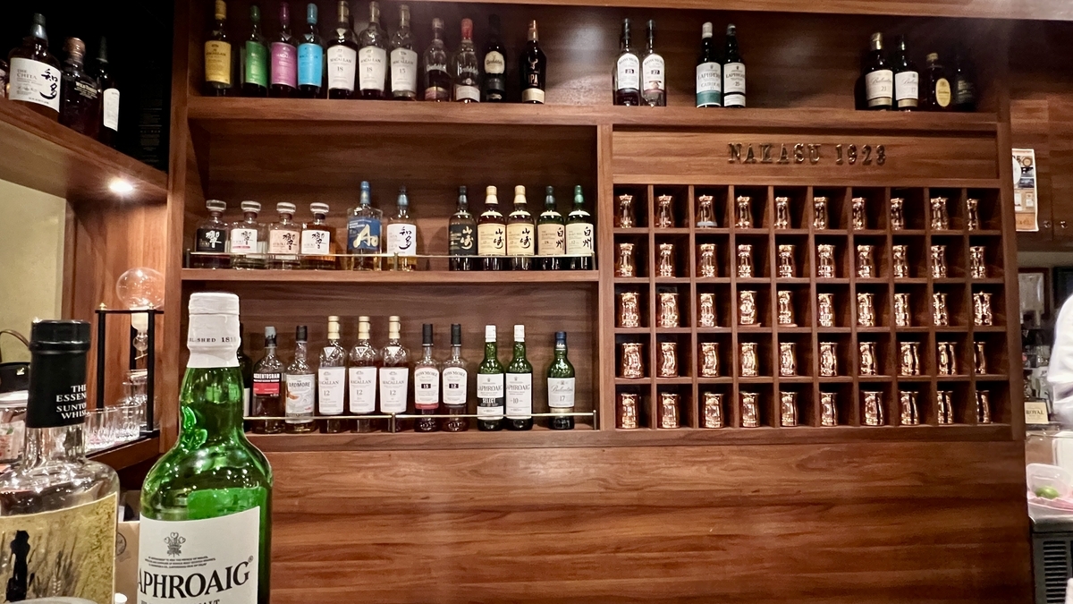 ボトル棚と銅製マグの壁面収納が並ぶハイボールバーのバックバー