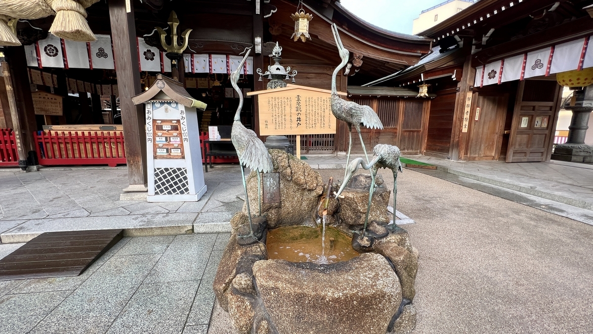 霊泉鶴の井戸の石組みと鶴の噴水像が並ぶ泉