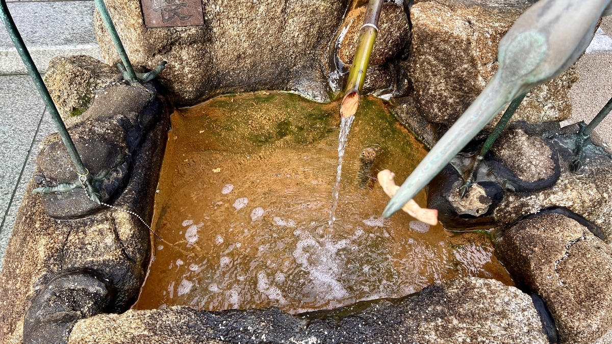 霊泉鶴の井戸の竹樋から落ちる湧水と茶色い水面
