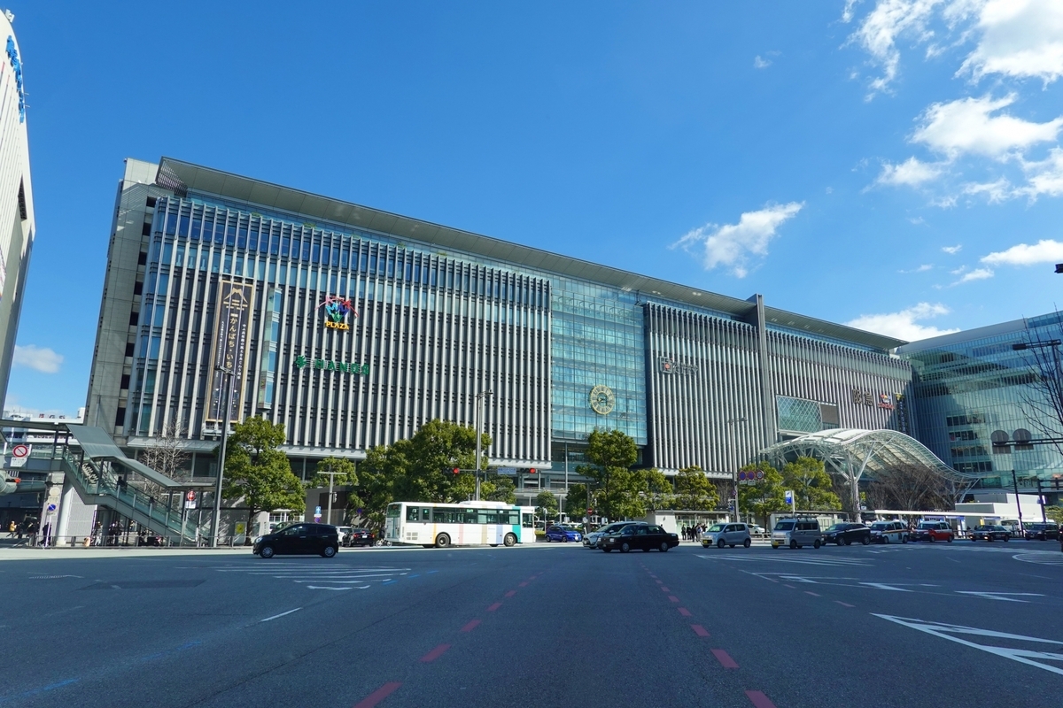 The glass and vertical louver facade of JR Hakata City station building with buses and taxis running under blue skies
