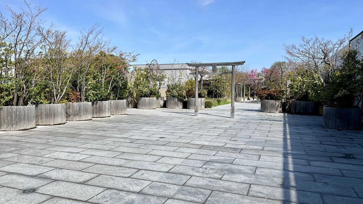 A wide stone-paved plaza in the rooftop garden with a wooden torii gate in the distance