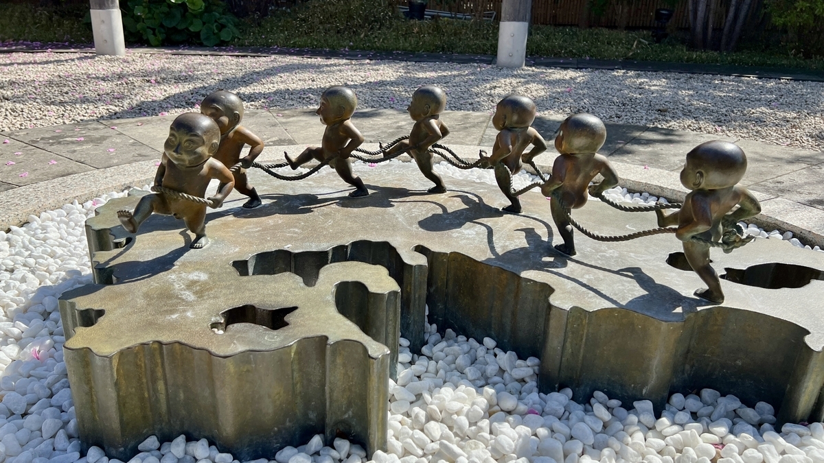 Bronze statues of seven children holding a rope in a circle on white gravel