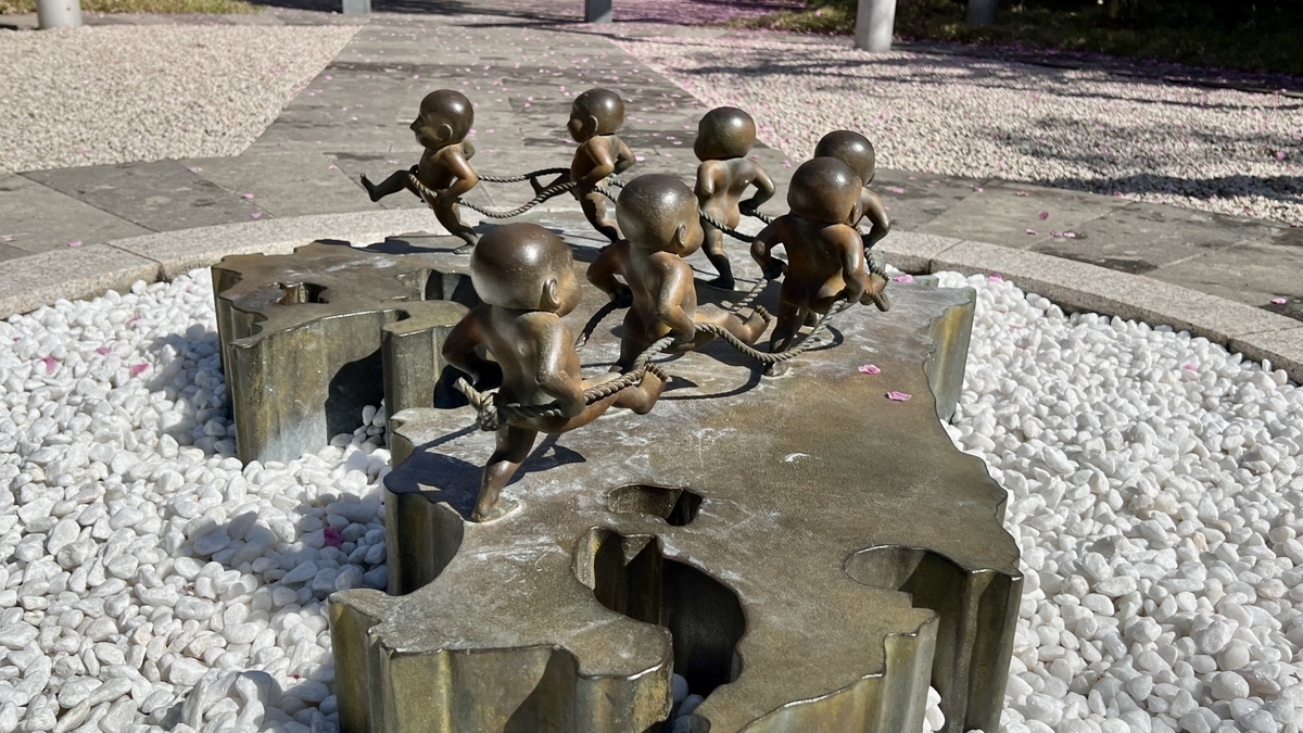 Seven children connected by rope circling a base shaped like the Japanese archipelago