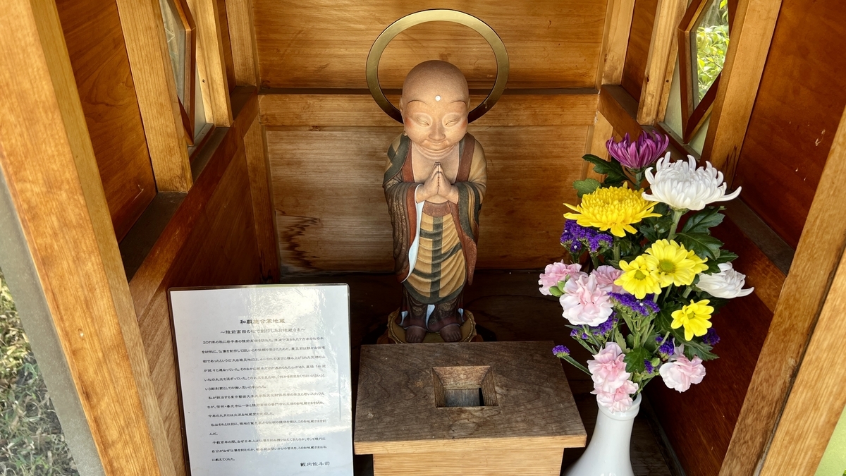 A praying Jizo statue enshrined in a wooden shrine with flower offerings