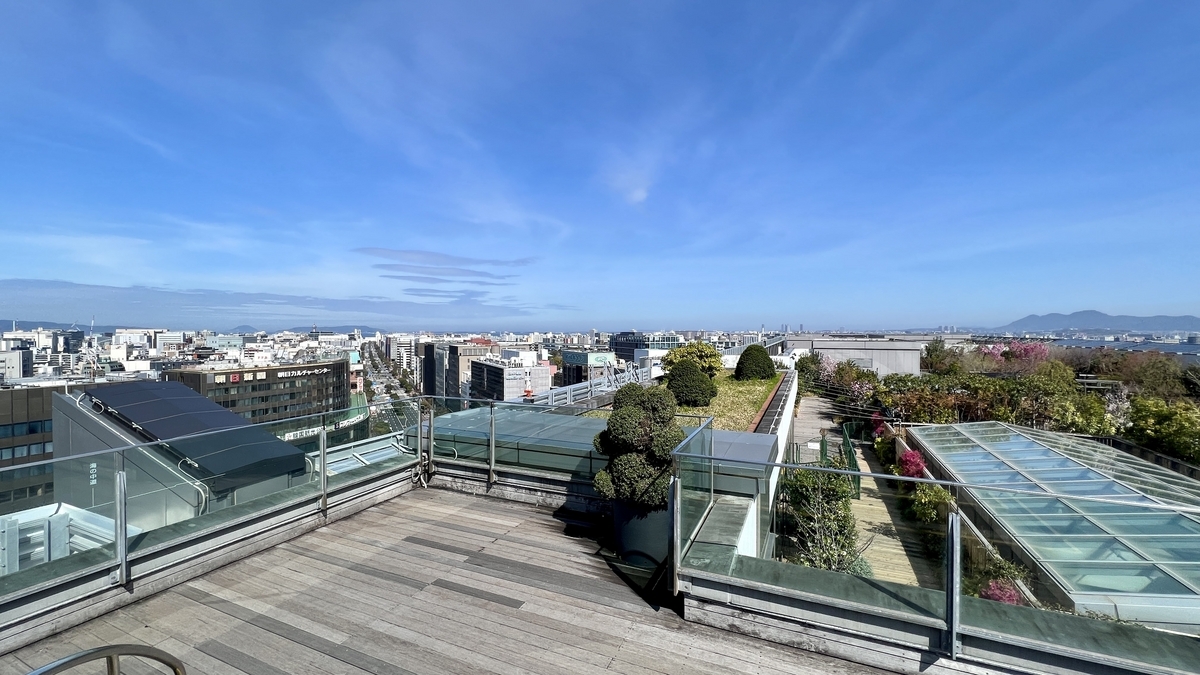 The wooden deck of Tsubame-no-Mori Hiroba and the Hakata cityscape through glass railings
