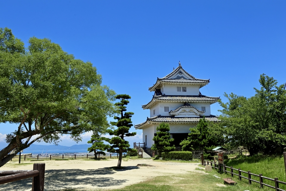 The main keep of Marugame Castle surrounded by greenery. The three-story structure shines under a clear blue sky.