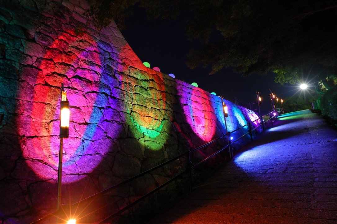 Colorfully lit stone walls of Marugame Castle during the night illumination event.