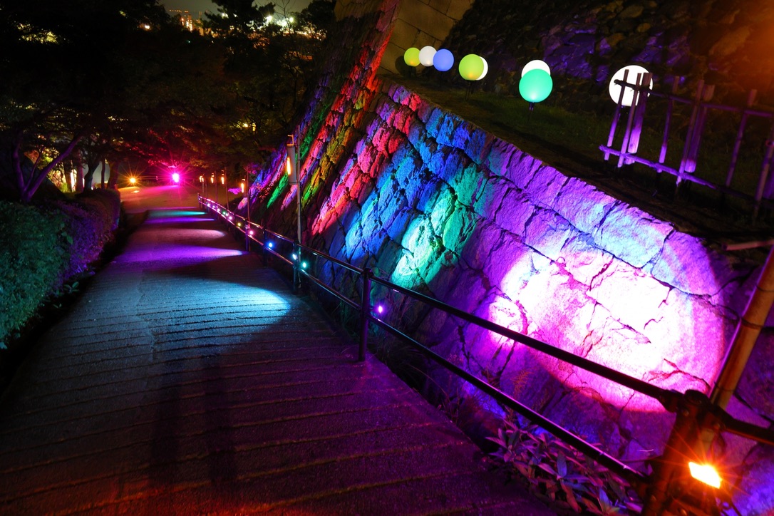 Stone wall illuminated with vibrant lights. The castle’s approach is bathed in a luminous glow.