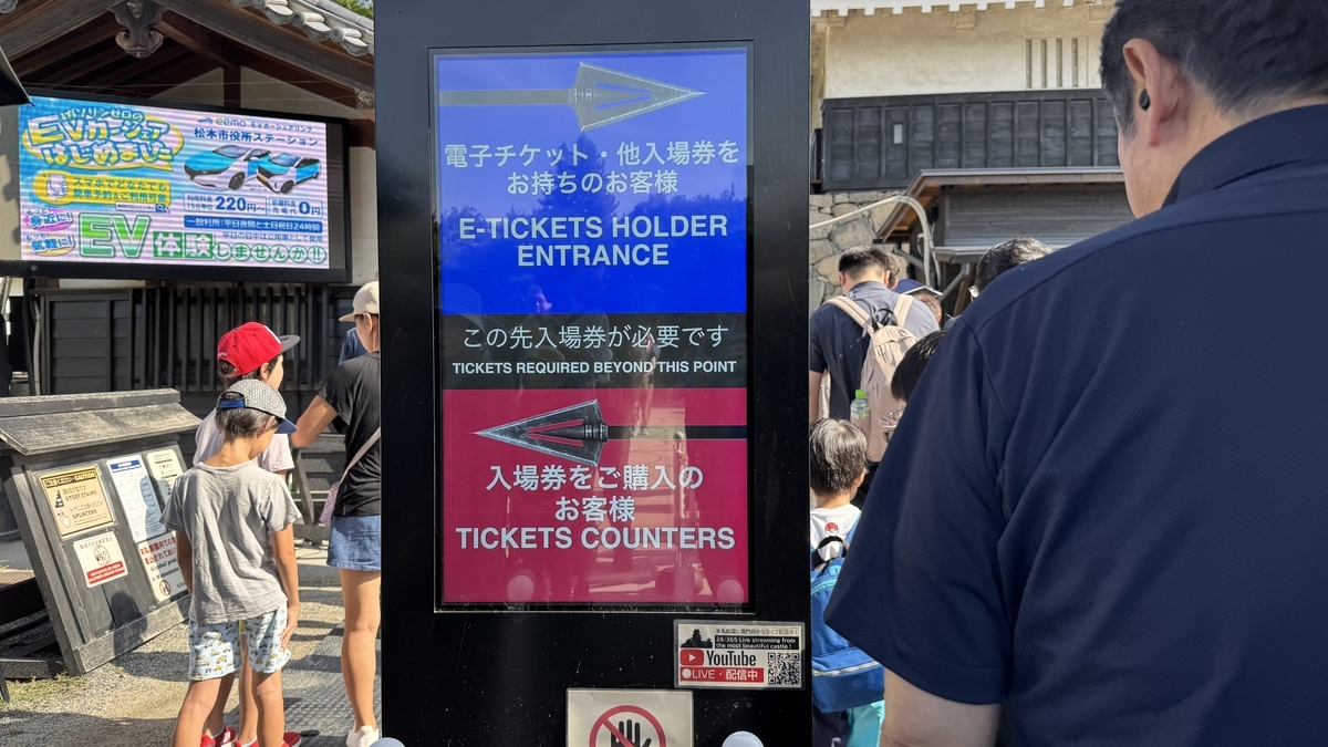 Signboard for electronic tickets at Matsumoto Castle with a line of visitors