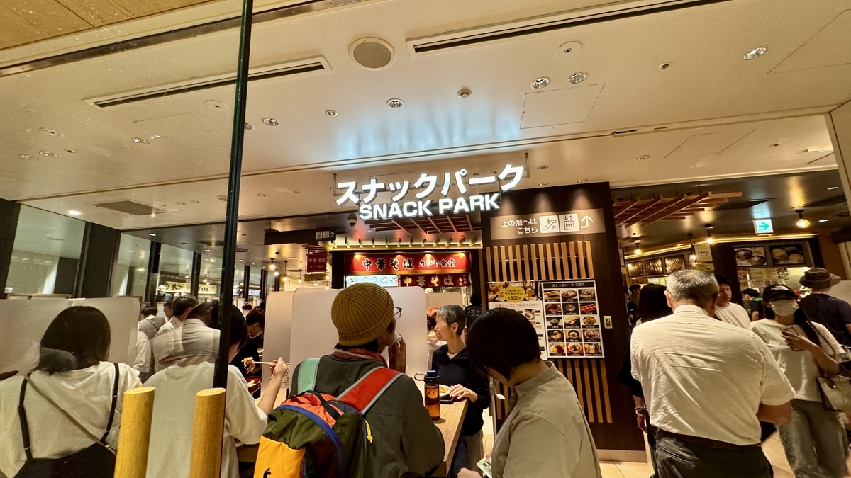 阪神梅田本店スナックパークの入口。白いロゴ看板の下に人々が集まる
