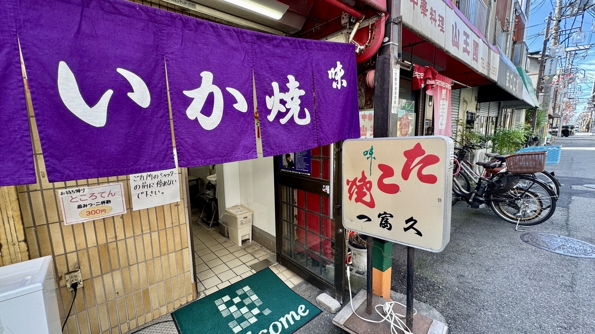 Red signboard for ika-yaki next to the entrance of Ichifuku and a close-up of the storefront