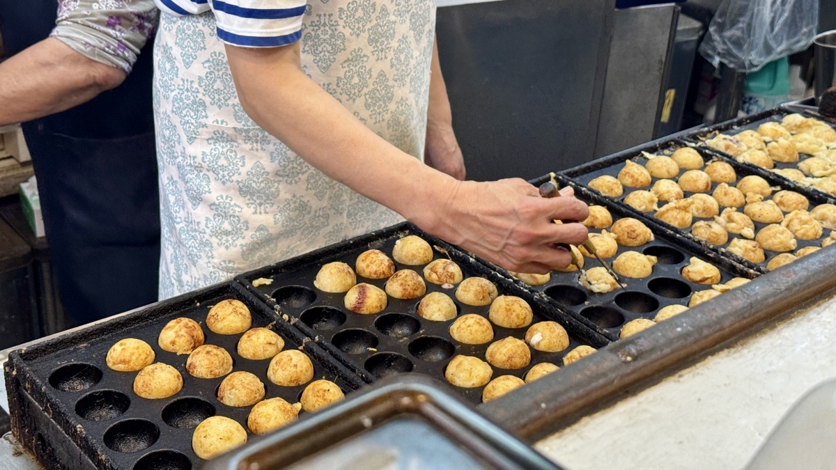 Close-up of staff grilling takoyaki on a hot iron plate inside the shop