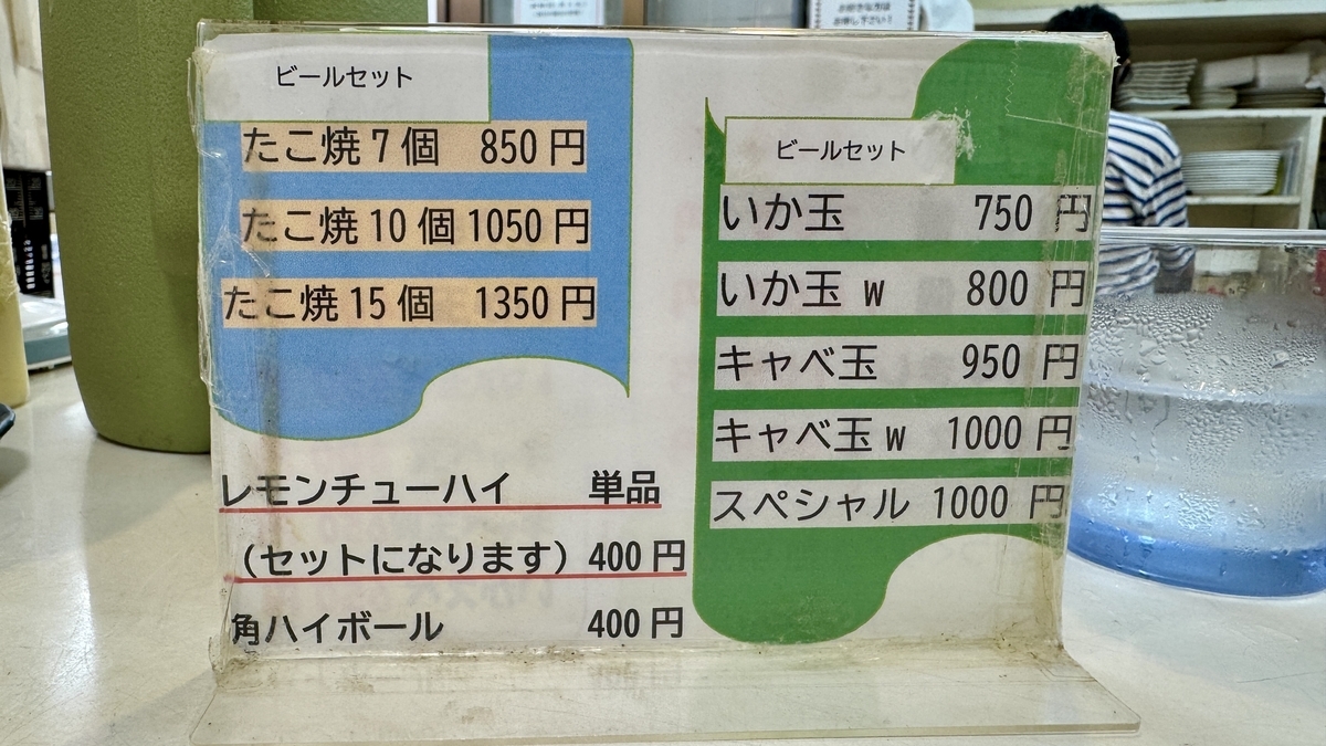 Drink menu board on the counter displaying prices for Lemon Chuhai and Highball