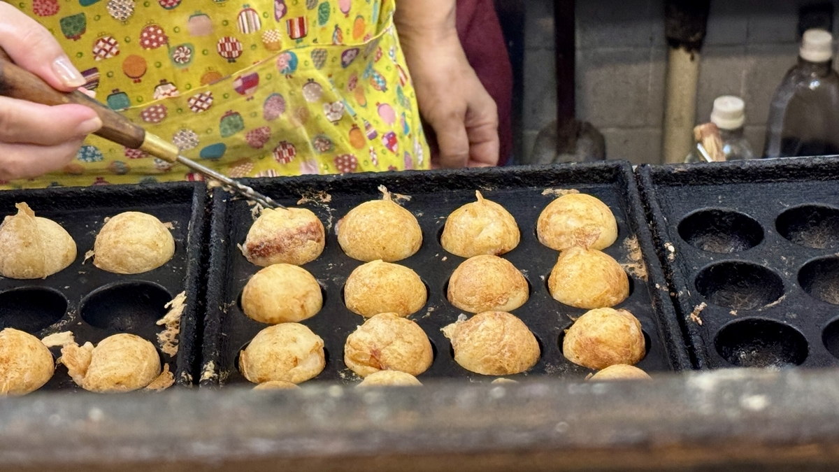 Staff carefully grilling takoyaki on a hot iron plate