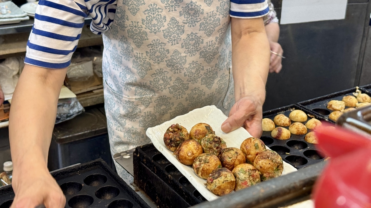 Owner transferring freshly grilled takoyaki onto a serving tray