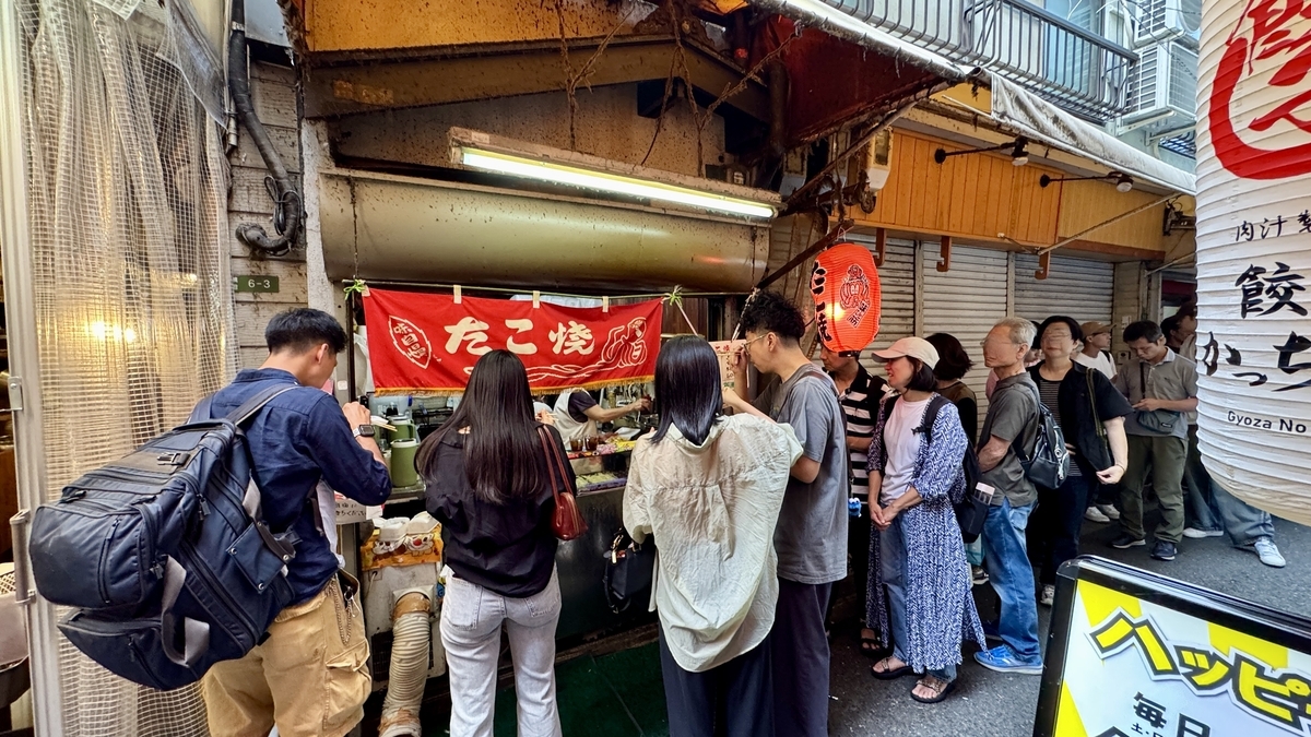 Exterior of Hiroko with people lined up and a red shop curtain swaying