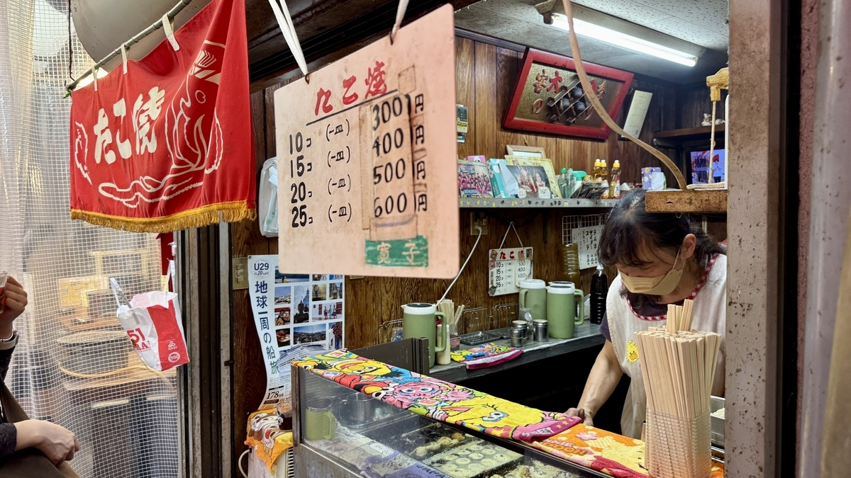 Close-up of the owner’s hands turning takoyaki on the griddle