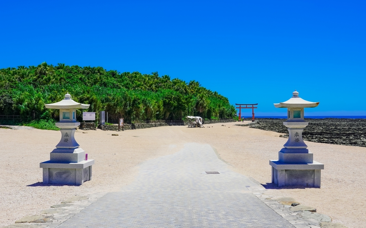 白砂の広がる海辺に小さく赤い鳥居が見える青島神社の参道風景
