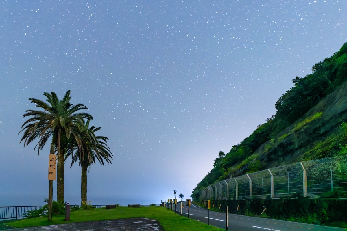 วิวกลางคืนของช่องเขาโฮริคิริ พร้อมท้องฟ้าที่เต็มไปด้วยดาวและต้นฟีนิกซ์ริมถนน