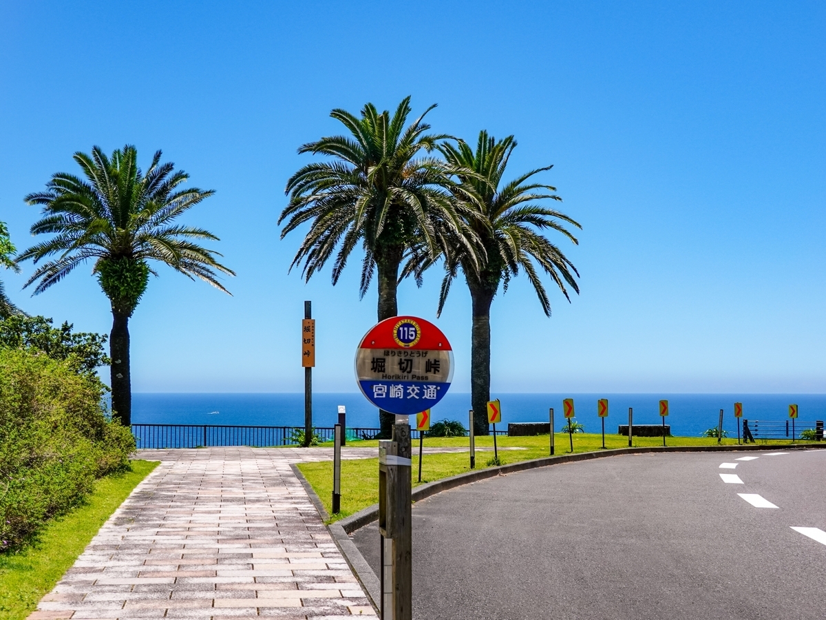 ป้ายรถบัสช่องเขาโฮริคิริ พร้อมฉากหลังเป็นต้นปาล์มและท้องทะเลสีน้ำเงิน