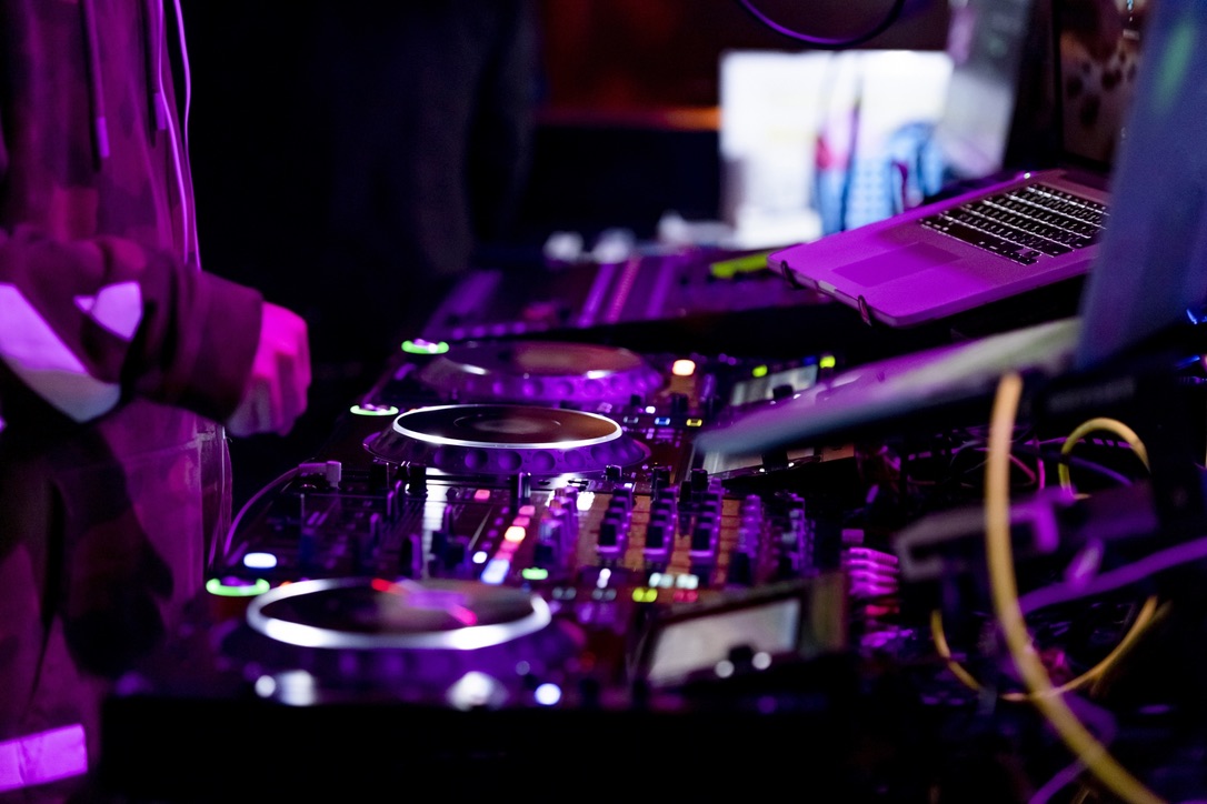 Cabina de DJ con manos operando una mesa de mezclas bajo luces iluminadas