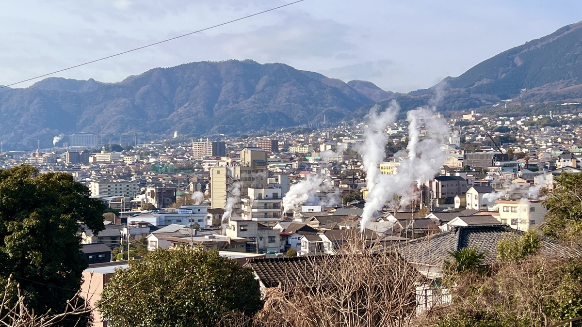 別府市街地に立ち上る温泉の湯けむりと背後に連なる山並みの景色