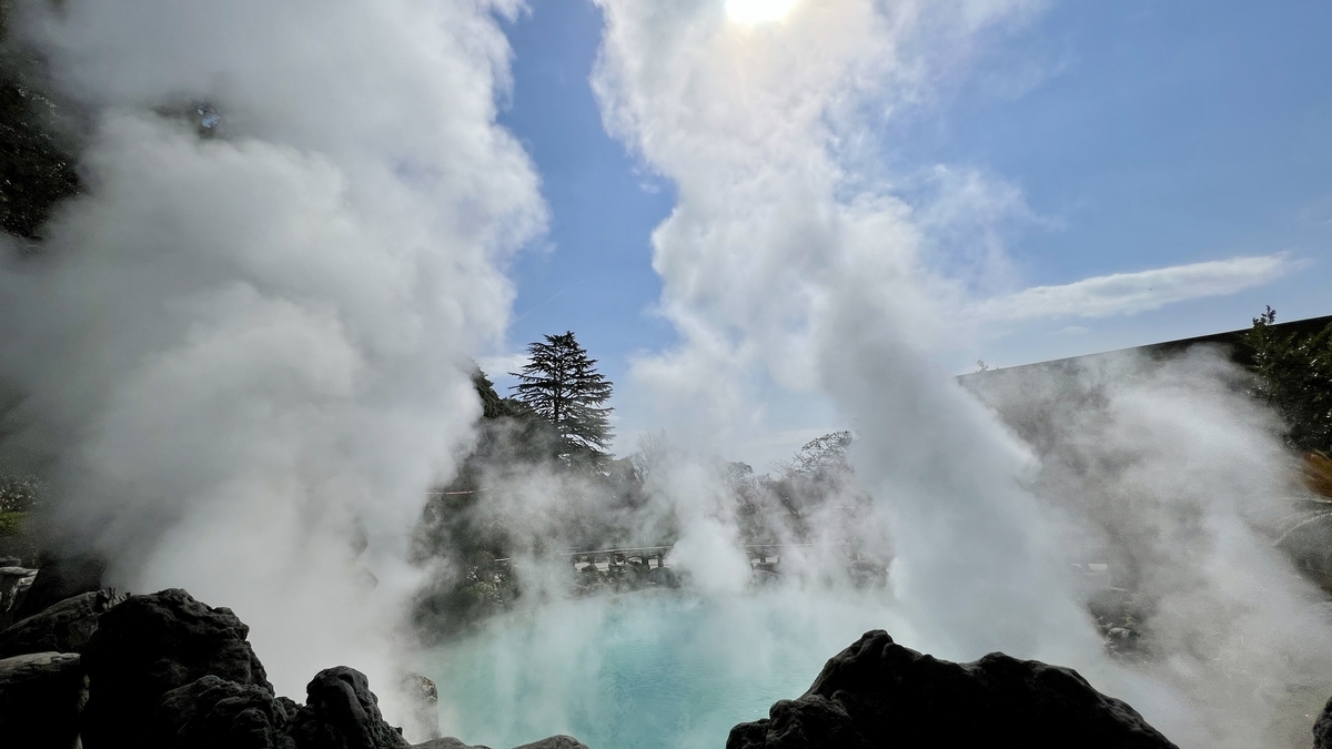 青い空の下で白い噴気が立ちこめる別府地獄めぐりの熱泉と湯だまりの風景