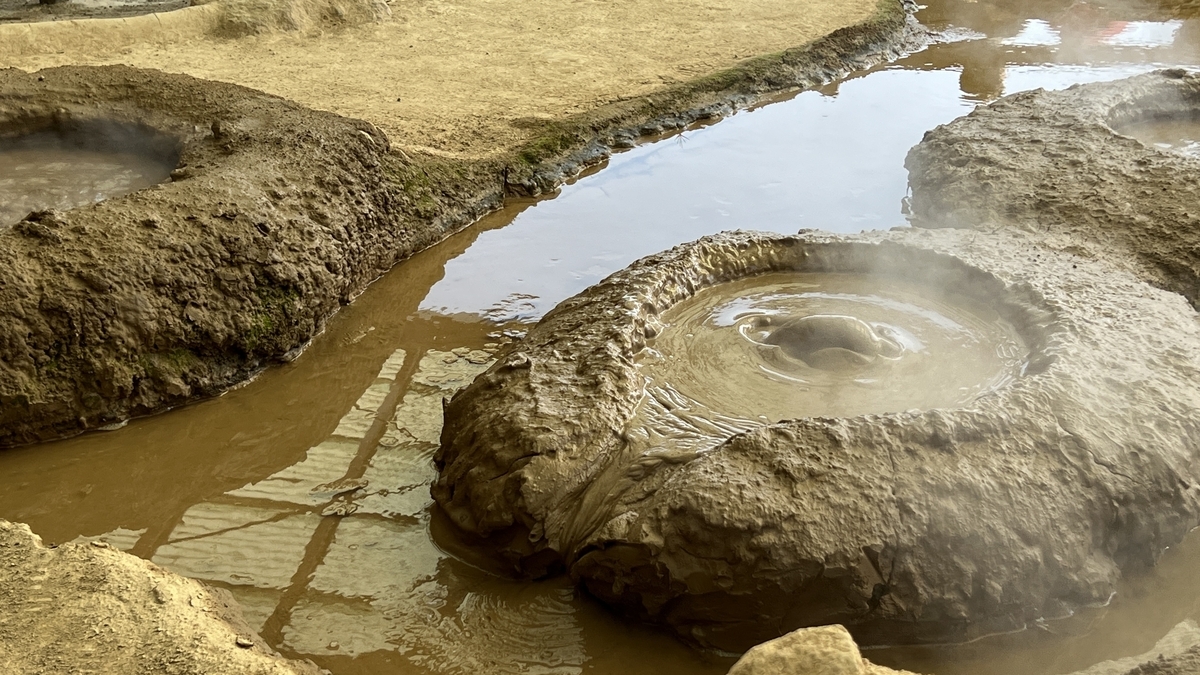 湯気が立つ泥の噴出口が泡を立てる地獄の熱泥と浅い水路の様子