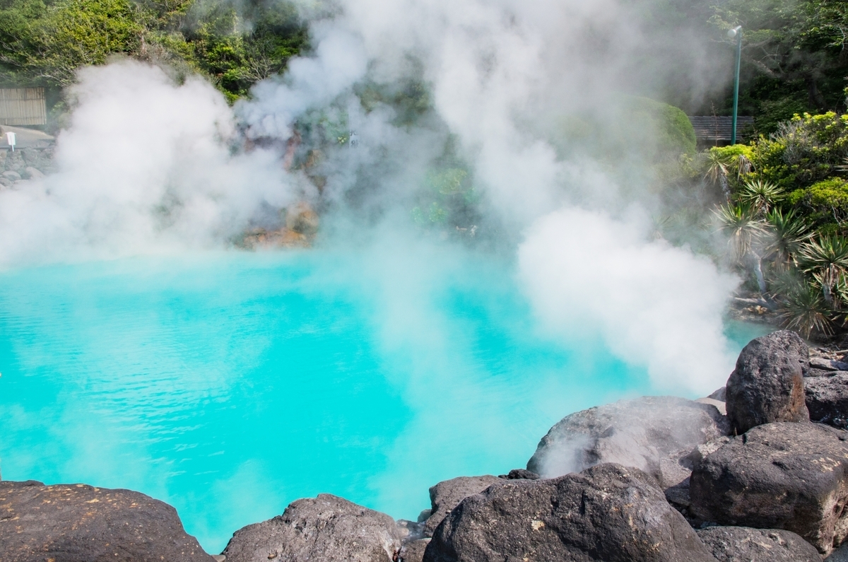 白い湯けむりが立つ鮮やかなコバルトブルーの海地獄の湯だまりと黒い岩肌
