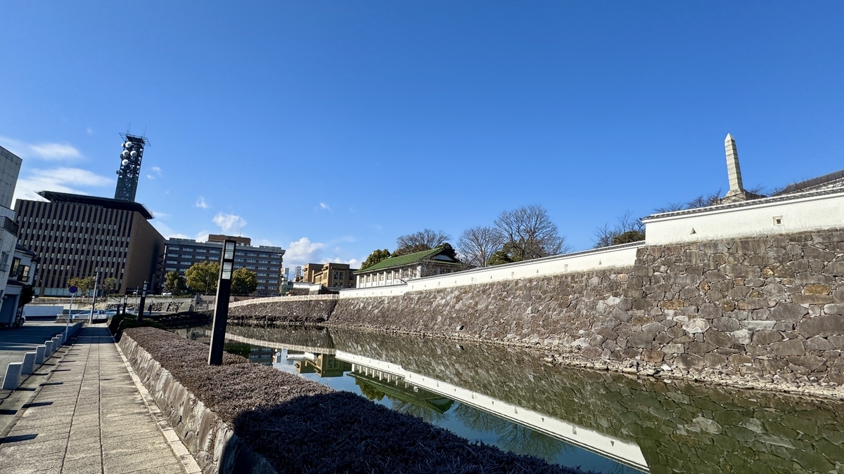 고후성의 흰 벽과 석축이 해자에 비치는 풍경, 산책로와 전파탑이 보이는 맑은 날 낮 풍경