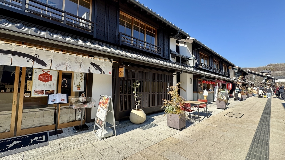 돌바닥 거리를 따라 늘어선 마치야 점포와 카페 메뉴 간판, 사람들이 오가는 긴 거리 낮 풍경