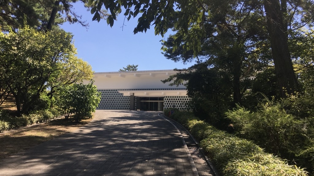 Museo Yamato Bunkakan de paredes blancas visible al final de un camino arbolado con luz filtrada