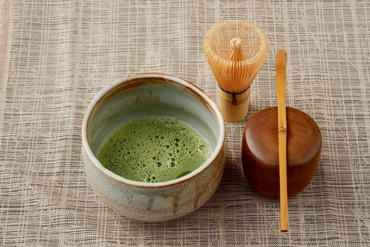泡立った抹茶が入った陶器の茶碗と竹の茶筅と木製の棗に置かれた茶杓