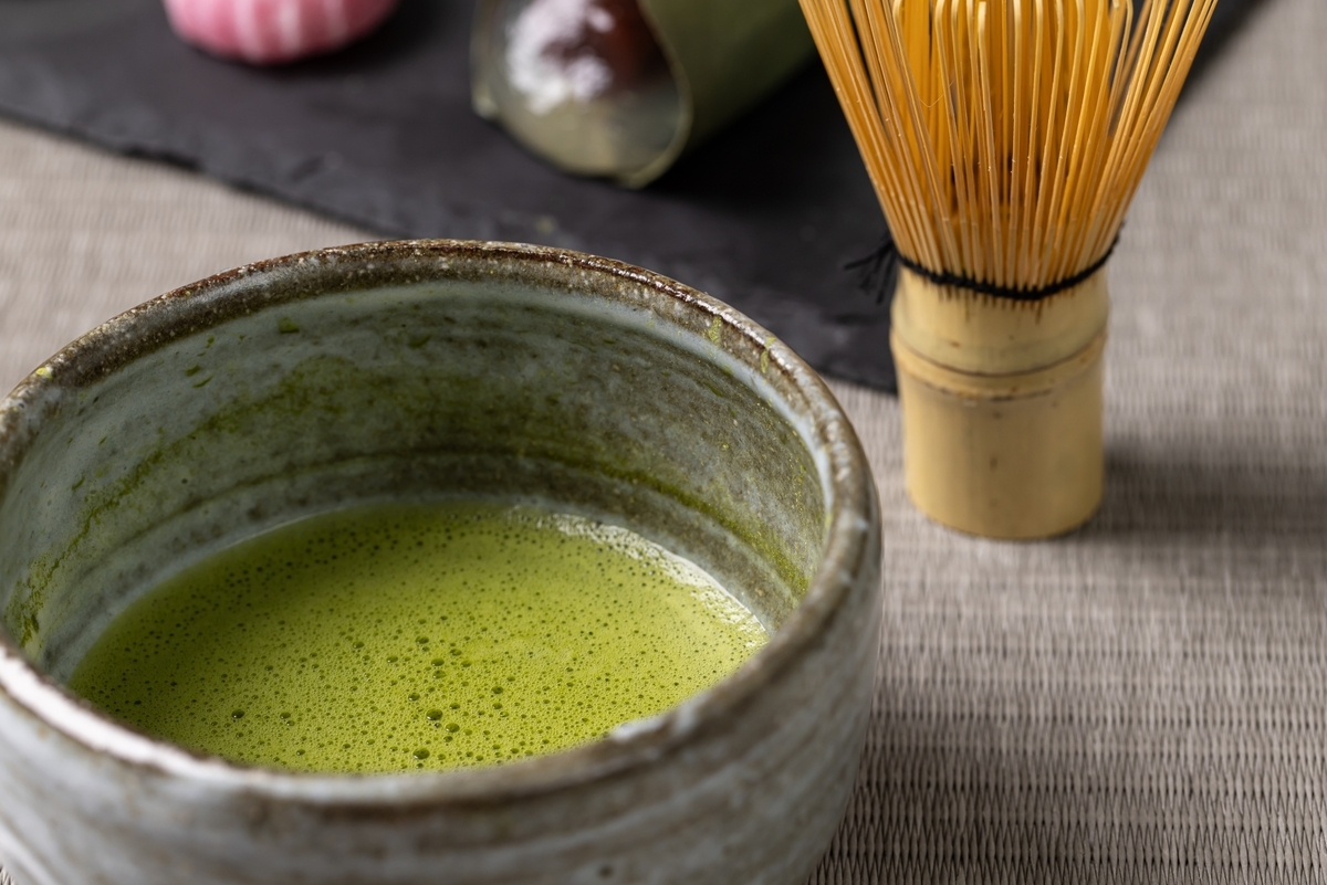 泡の浮いた抹茶が入った釉薬の茶碗と背後に置かれた竹の茶筅