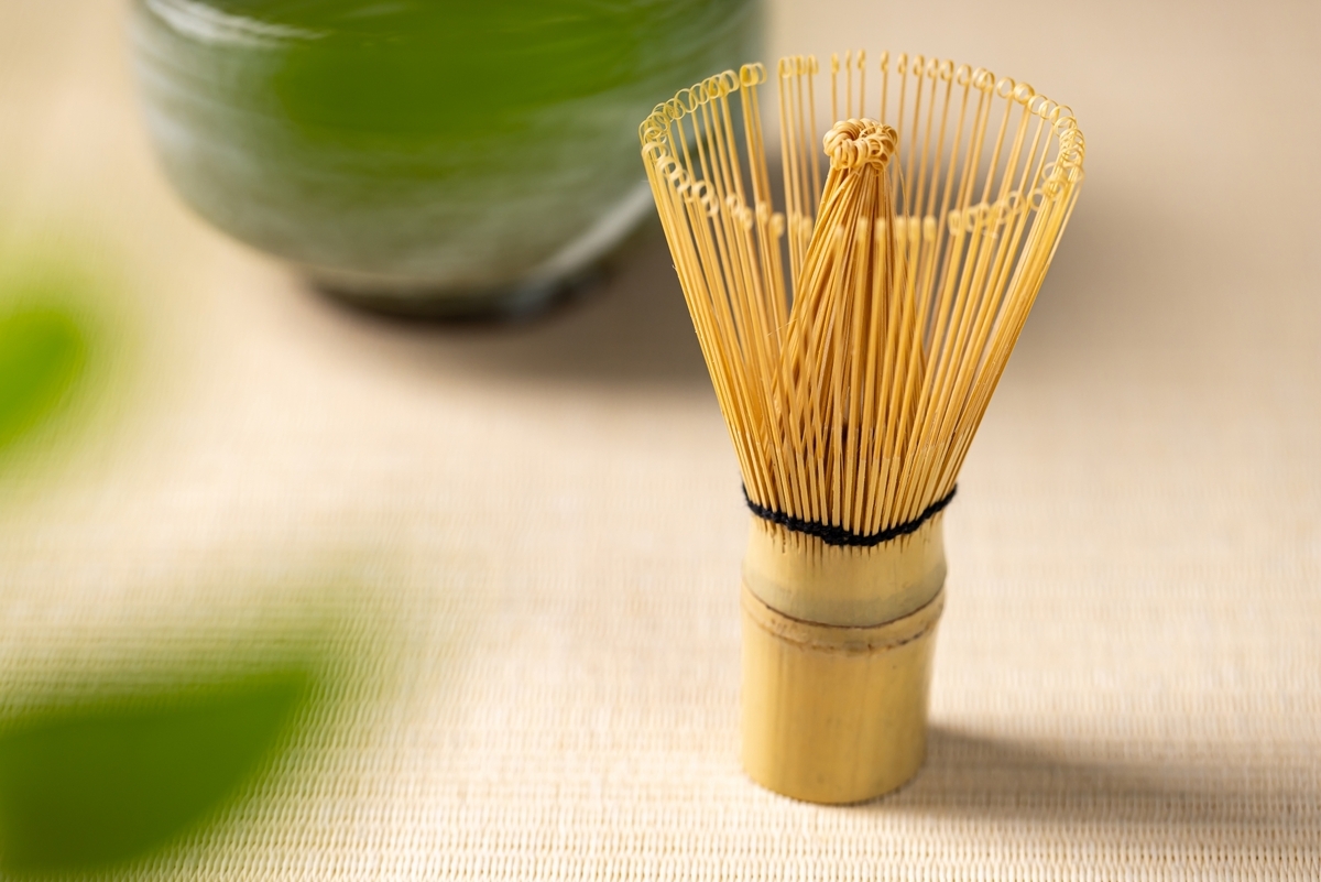 竹の穂先が広がった茶筅のクローズアップと背景にぼけた抹茶茶碗